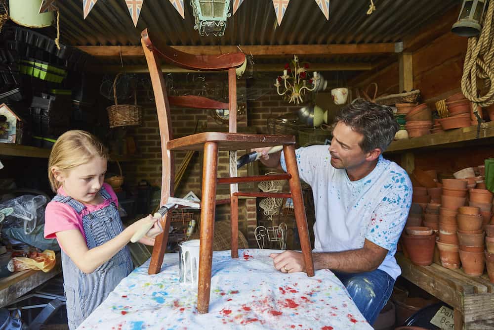 Father and daughter painting chair in workshop