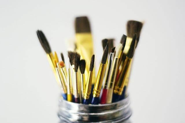 Glass jar holding numerous various paint brushes