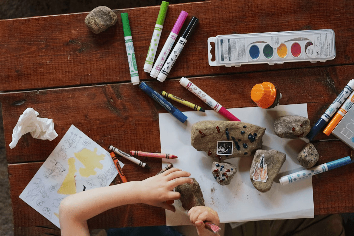 Child painting rocks with crayons and markers, a